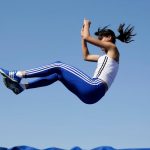 Female athlete in mid-air during athletic jump with blue sky background.