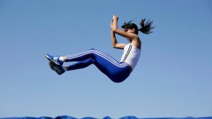 Female athlete in mid-air during athletic jump with blue sky background.